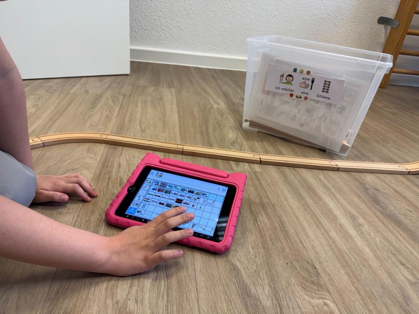 Kinderhand tippt auf einem Tablet neben einer Holzeisenbahn