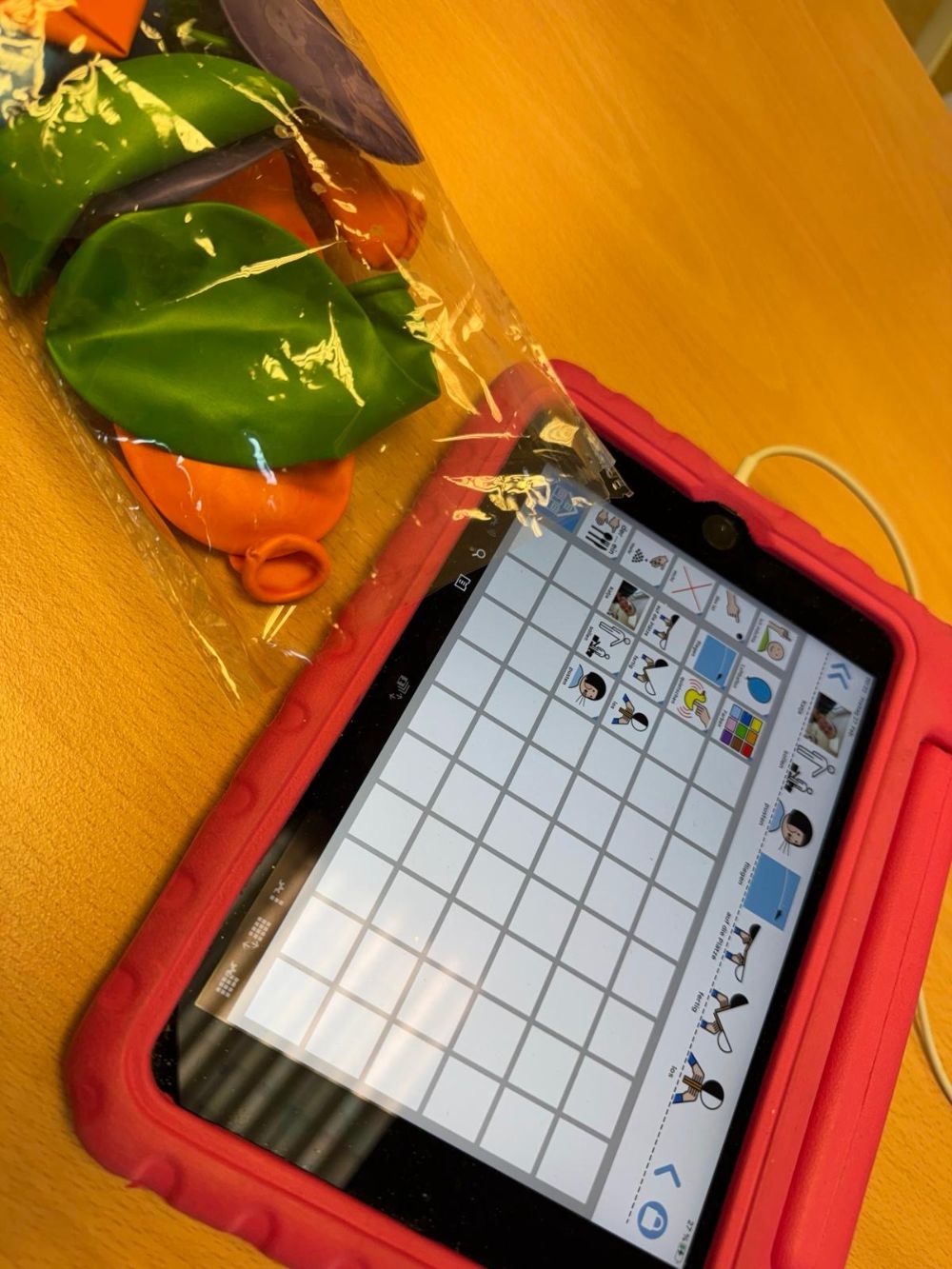 Luftballons neben einem Tablet in roter Schutzhülle mit Symbolen wie „pusten“ und „fliegen“