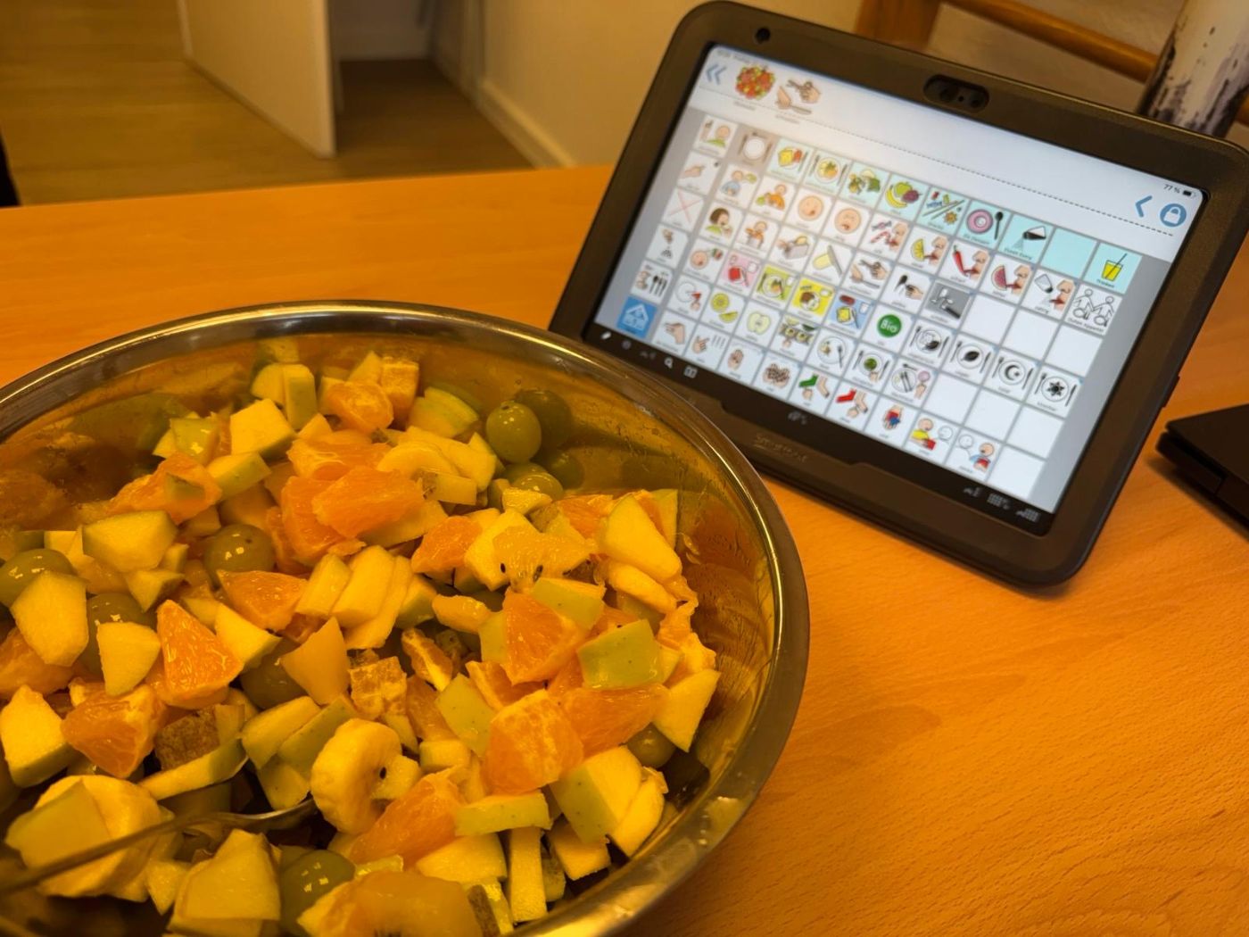 Schüssel mit Obstsalat, daneben ein Talker mit Symbolen zum Thema Essen