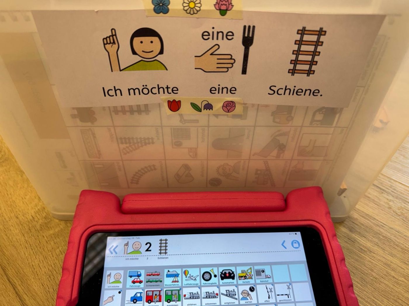 Symbolsatz „Ich möchte eine Schiene“ auf einer Box, davor ein Tablet mit demselben Satz